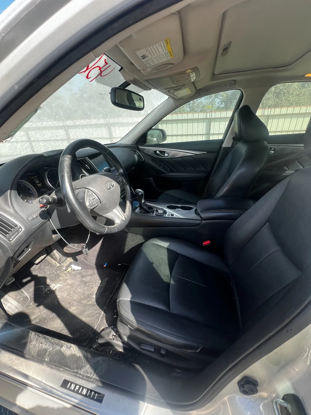Front cabin of the Q50 showing a dirty black leather driver seat, dusty steering wheel and key on a tag