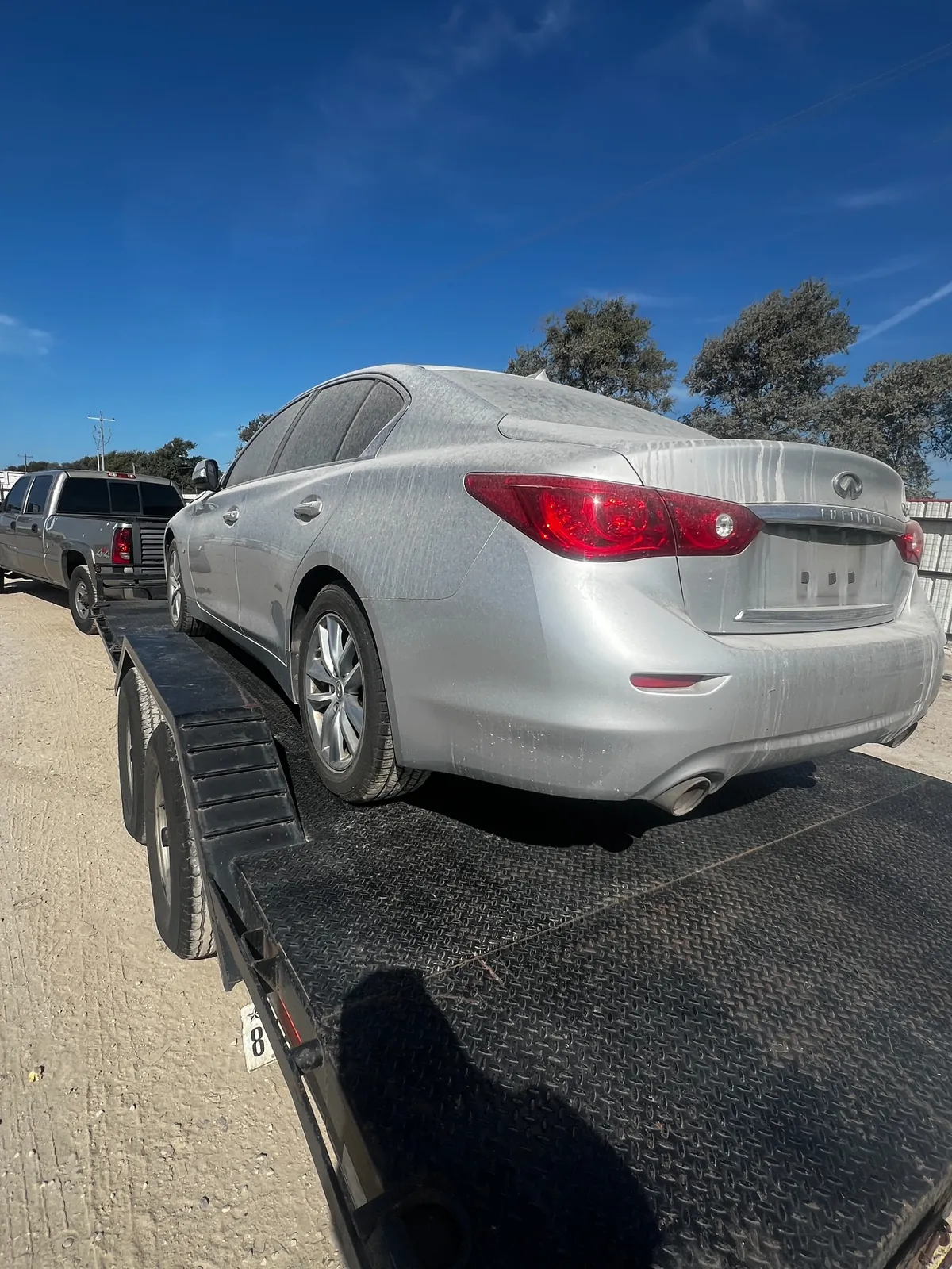 Rear view of the silver Q50 on the trailer with a heavy layer of dust across the roof, glass and tail lights