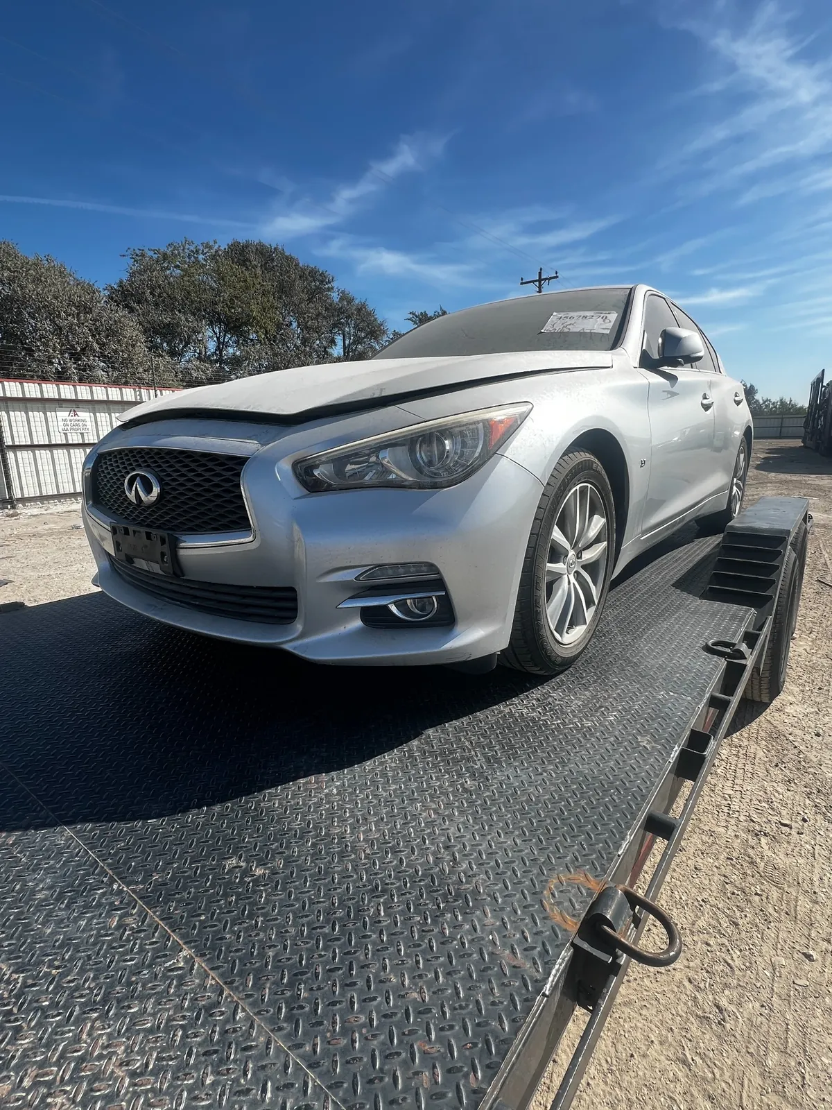Front three-quarter view of the silver Q50 on the trailer with the hood sitting slightly raised and factory alloy wheels fitted